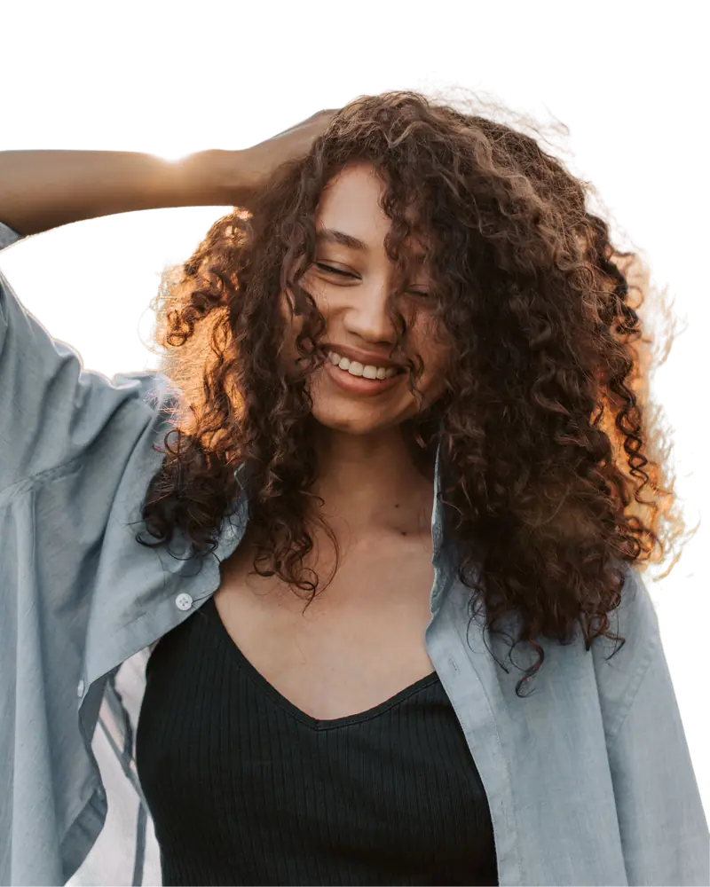Woman with curly hair smiling outdoors with the background removed